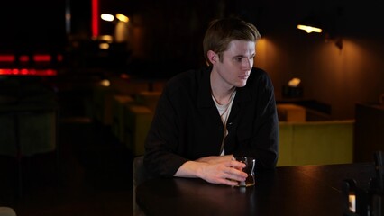 Young man drinking whiskey while sitting in a restaurant in the evening and feeling lonely. Lifestyle, loneliness concept.
