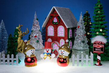 Three snowmen among glass Christmas trees near a red Christmas house surrounded by a fence