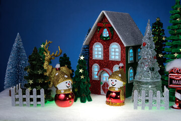 Two identical snowmen among the fir trees near a red Christmas house surrounded by a fence