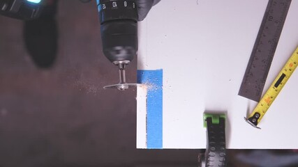 Close-up of a worker using a circular saw attachment on a drill to cut a white wooden board