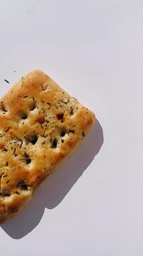 a square piece of golden focaccia bread with a soft dimpled surface and scattered rosemary resting against a clean white background.