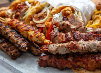 Mixed grilled meat platter, meat skewers, kebab pieces, and blur gyro wraps background, closeup