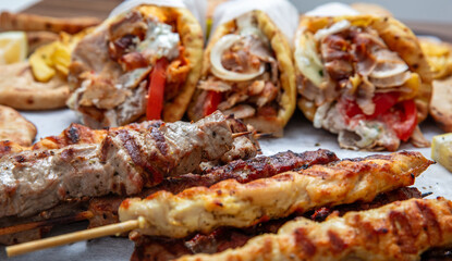 Mixed grilled meat platter, meat skewers, kebab pieces, and blur gyro wraps background, closeup