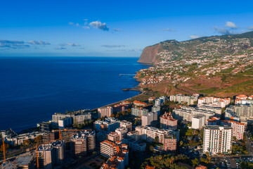 Fototapeta premium Aerial view of Funchal, Madeira, Portugal, with terraced hills, high rise hotels by the promenade, a curving bay, and late day light over deep blue Atlantic waters.