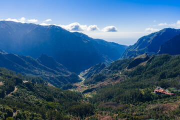 Fototapeta premium Aerial view shows a deep valley on Madeira Island, Portugal, near Pico do Arieiro and Curral das Freiras. Evergreen forests line steep ravines under crisp midday light.