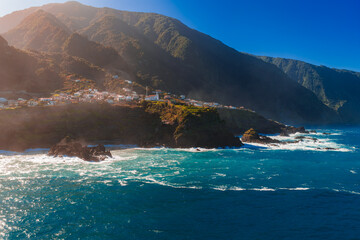 Small whitewashed village on rugged cliffs in Madeira, Portugal. Late afternoon light warms the scene as deep blue waves crash on black volcanic rocks and headlands. © Aerial Film Studio