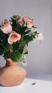 A calm floral arrangement featuring blush roses, white blooms, and layered greenery placed in a warm-toned clay vase against a clean, minimal background.