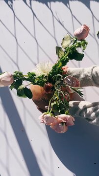 A delicate arrangement of blush pink roses and a white chrysanthemum resting in a rustic clay vase, accented by natural greenery and soft directional sunlight that creates gentle shadows and a calm, o