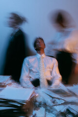 motion core editorial shot, model in white shirt and tie sitting calmly on messy office desk, piles of documents around, blurred figures walking fast in background, surreal fashion alethic