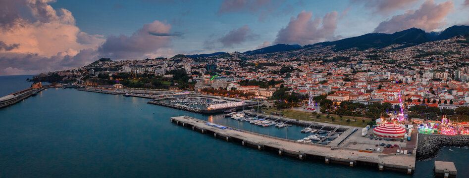 Aerial twilight view of Funchal, Madeira, Portugal, with Marina do Funchal, cruise pier, festive waterfront lights, whitewashed roofs, Se Cathedral area, Avenida do Mar.