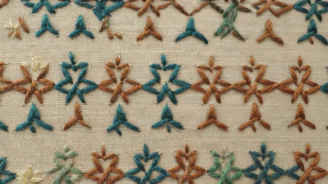 Detailed close-up of intricate blue and brown thread embroidery on linen fabric, showcasing traditional textile craftsmanship and decorative stitching.