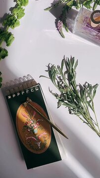 a calm still life arrangement featuring a vintage floral notebook, a gold pen, fresh and dried herbs, and soft natural light creating a serene and thoughtful atmosphere