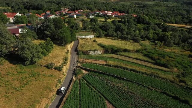 A camper minibus drives through a mountain village on a narrow serpentine road. Northern Portugal.
