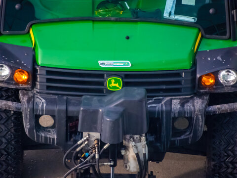 Calgary, Alberta, Canada. Dec 12, 2025. A close-up shot of a green John Deere Gator UTV's front grille featuring the logo and complex hydraulic and electrical connections below the bumper.