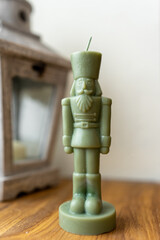 Green nutcracker candle figurine on wooden table with rustic lantern 
