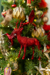 Sparkling red reindeer ornament on holiday Christmas tree with golden decorations
