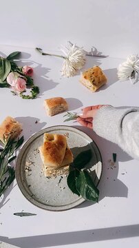 rustic tabletop scene featuring rosemary focaccia bread on a ceramic plate surrounded by soft florals scattered crumbs and gentle natural light shadows