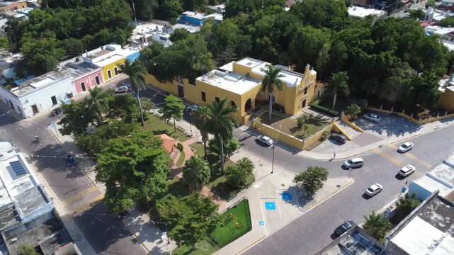 Commercial 4K drone pan shot with smooth lateral movement over an urban park and historic church surroundings in M&eacute;rida, Yucat&aacute;n, highlighting everyday city life and tropical scenery.