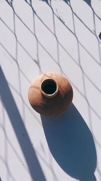 A simple round ceramic vase viewed from above, resting on a white surface with gentle diagonal shadows that highlight its natural clay texture and minimalist form.
