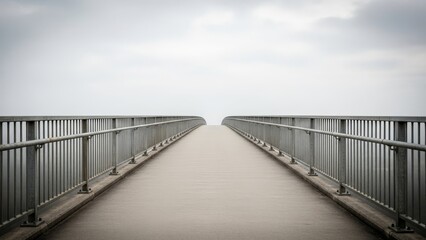 Fototapeta premium Misty pedestrian bridge with metal railings under an overcast sky, creating a symmetrical perspective.