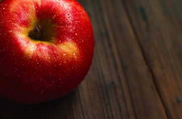 Wet red apple resting on dark wooden planks, highlighting freshness, healthy eating, and natural ingredients