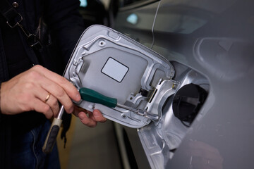 Workshop technician carefully inspecting fuel hatch with tools nearby, Professional mechanic thoroughly examines internal fuel cover of vehicle during maintenance