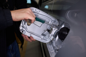 Workshop technician carefully inspecting fuel hatch with tools nearby, Professional mechanic thoroughly examines internal fuel cover of vehicle during maintenance