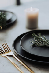 Minimalist holiday table with matte black plates, gold cutlery and a single candle