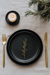 Minimalist holiday table with matte black plates, gold cutlery and a single candle