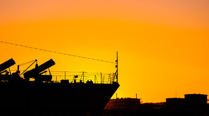 Silhouetted bow of naval vessel with missile launchers at vivid sunset.