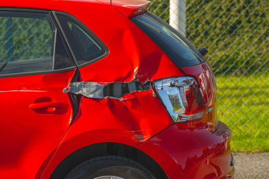 Red compact car with significant rear side collision damage parked outdoors.
