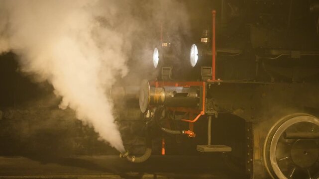Front of a vintage steam locomotive releasing dense white steam, headlights glowing through the haze, metal details and pipes visible, creating a dramatic, atmospheric scene suited for cinematic slow
