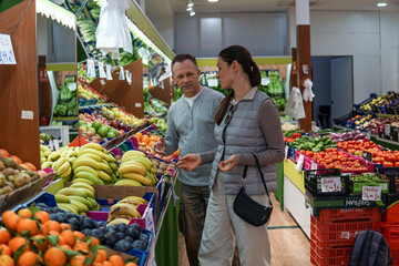 middle-aged man and woman buying fruits and vegetables at an outdoor market