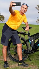 Obraz premium Active senior man enjoying outdoor cycling on an electric mountain bike, capturing a joyful moment with his smartphone, embracing a healthy and adventurous lifestyle in a park
