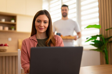 Woman working on laptop getting breakfast from partner