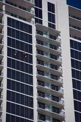 Modern High-Rise Building With Glass Facade And Rappelling Window cleaners Workers On A Clear Day in St. Petersburg, FL. Expansive glass panels and stacked balconies. Two workers in safety gear descen