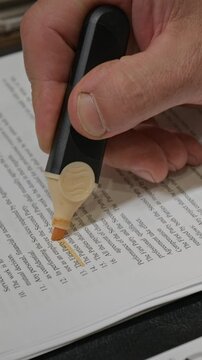 Vertical close-up of hand of anonymous male lawyer or businessman analyzing contract or commercial agreement, highlighting terms and material clauses using yellow marker, while working in office