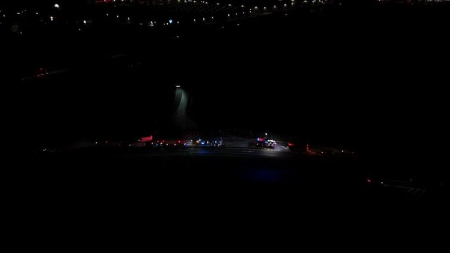 Drone night video of emergency services responding on a road, with ambulance, firefighters and police assisting at an incident scene, flashing lights highlighting rescue operations and public safety.