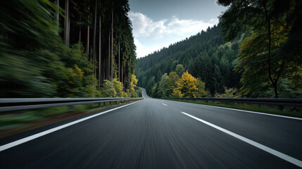 Empty road through forest with motion blur highway asphalt curve guardrail evergreen deciduous autumn tree pine perspective vanishing point long exposure motion speed travel scenic rural landscape