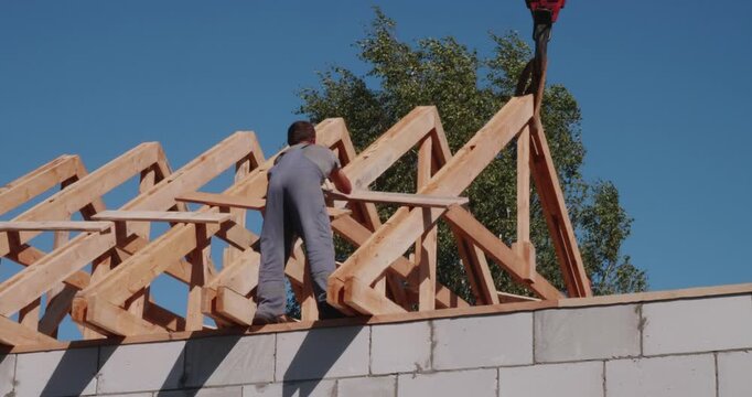 Professional construction worker assembling the wooden roof frame on a new house building against a clear blue sky, showing the process of residential property development.