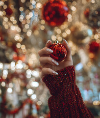 Female hand holding red Christmas ornament with festive bokeh lights