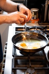 mans hand cracking a egg in to a fry pan cooking in the kitchen