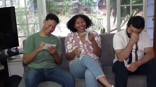 Multicultural friends sitting on a sofa playing a fun guessing game and celebrating a victory at home