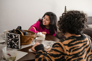 Mother and daughter are sitting at a table with a variety of cups and a handbag