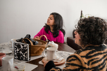 Mother and daughter are sitting at a table with a variety of cups and a handbag