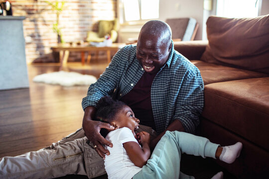 Senior grandfather and child granddaughter laughing on living room floor