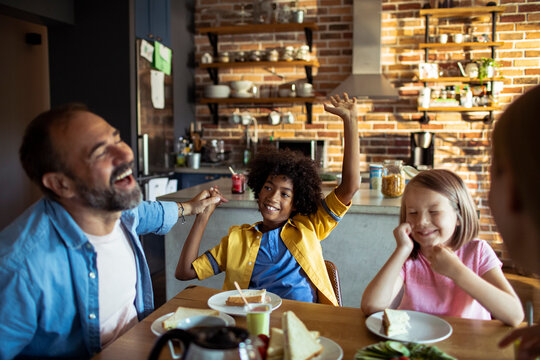 Adult father and children laughing at breakfast in home kitchen