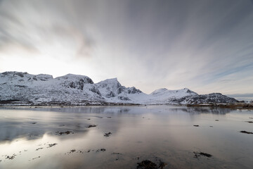 Late afternoon in Flakstad, Lofoten, Norway with snowy mountains reflected in still water