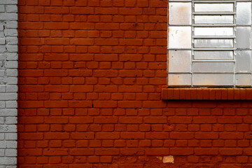 Textured facade of an old building featuring a vibrant red brick wall, a contrasting white painted section, and a multi-paned frosted window with a brick sill. Industrial urban architecture detail.