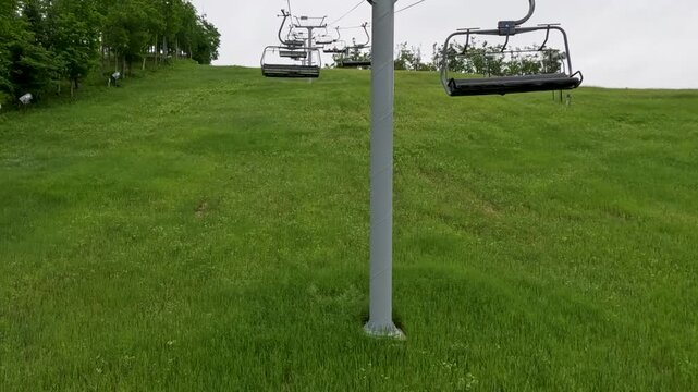 Riding on a Ski Lift in Summertime. Personal perspective taking off on a chair lift moving up the mountain. A grassy valley is below and a forest of green trees surround the scene. Northern Michigan.